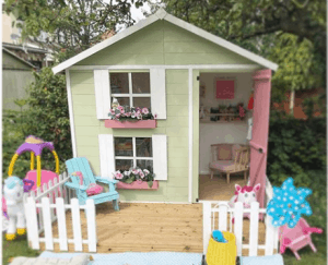wooden playhouse with two-storey windows and shutter and white picket fence with children's toys